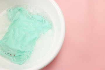 Baby clothes in washing basin on pink background, top view. Space for text