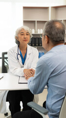 Asian female doctor and patient talking about something while sitting at the table, female doctor wearing white uniform and a stethoscope is checking the condition of an elderly male patient.