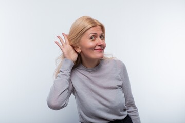 Mature blond woman dressed in a gray jacket eavesdrops and smiles