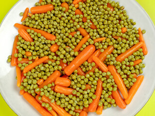 assiette de petits pois et carottes cuit, en gros plan, sur un fond jaune