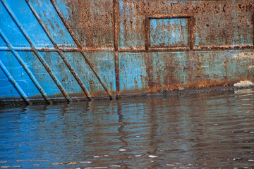 Rusty structure on a blue abandoned ship hull in a harbor