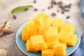 Dried mango cubes on blue plate on brown concrete, side view, selective focus.