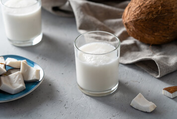 Two glasses of fresh coconut milk next to a blue plate of coconut pieces, emphasizing natural and healthy refreshment.