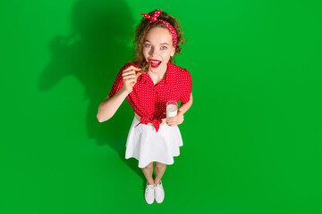 Full length photo of lovely young lady top view bite cookie milk glass dressed stylish red retro garment isolated on green color background