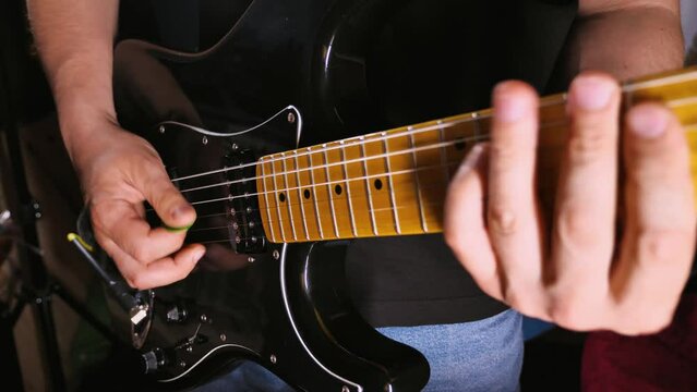 A musician's hands play a black electric guitar. Guitarist practising in a rehearsal base, garage or basement. Rock guitarist