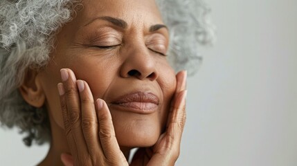 Close-up of a serene senior woman with closed eyes, gently touching her flawless skin, radiating confidence and beauty