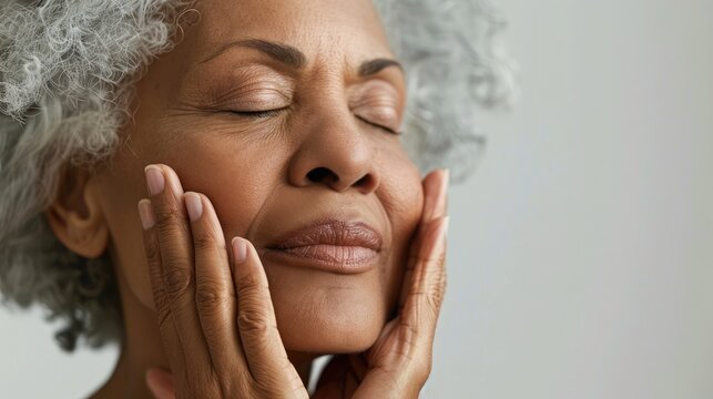 Close-up of a serene senior woman with closed eyes, gently touching her flawless skin, radiating confidence and beauty