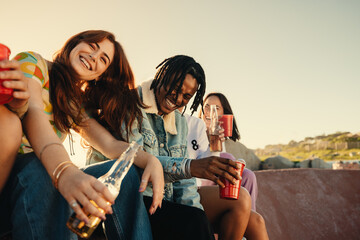 Obraz premium Happy young friends laughing and enjoying drinks outdoors on a sunny day