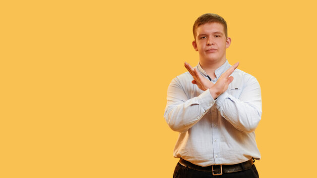 Stop gesture. Protest sign. Refusal act. Overweight dissatisfied man crossing hands warning expressing negation renouncement sign isolated on yellow empty space background.
