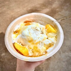 Sweet shaved ice with mang fruit and milk topping flavor. Cold fresh summer food isolated on outdoor stone ground flooring background.