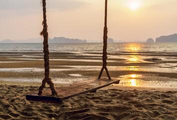 Big wooden swing on the beach with ocean on background at sunset time. Relaxing, peaceful vacation scene at the beach. Golden hour beach scene, Krabi, Thailand.