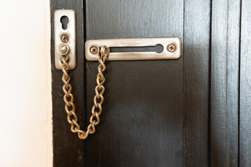Stainless steel door safty chain on locked mocca color door for security at hotel room.