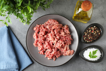 Raw ground meat, spices, parsley and oil on grey table, flat lay