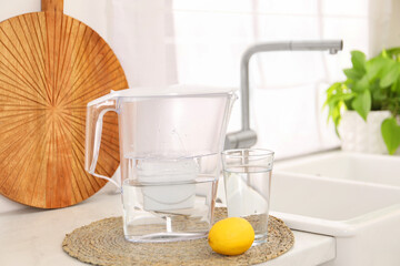 Water filter jug, glass and lemon on countertop in kitchen