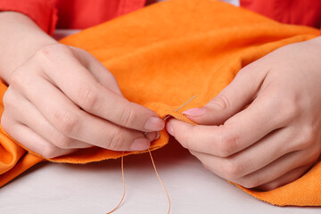 Woman sewing cloth with needle at light wooden table, closeup