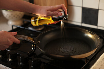 Vegetable fats. Woman sprinkling oil into frying pan on stove, closeup