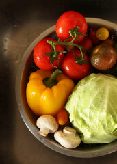 Different wet vegetables in metal colander inside sink, top view