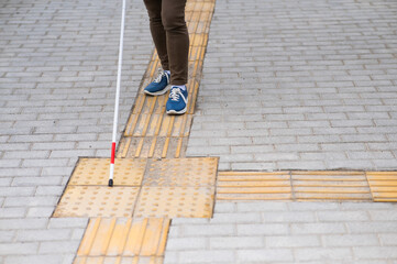 Close-up of a woman's legs with a cane near a tactile tile.