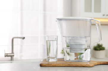Water filter jug and glass on light table in kitchen. Space for text