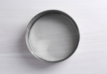 One metal sieve on white wooden table, top view