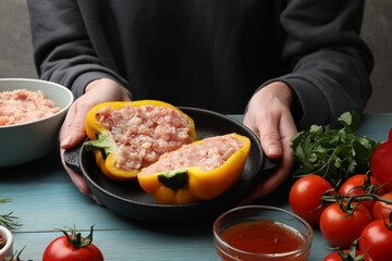 Woman making stuffed peppers with ground meat at light blue wooden table, closeup