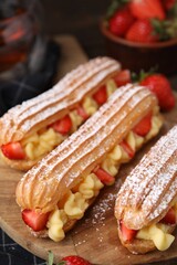 Delicious eclairs filled with cream and strawberries on table, closeup