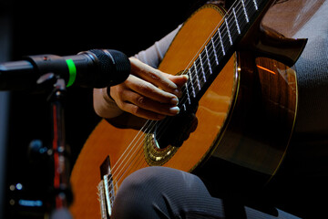 close up guitar neck and strings with mic on stage, beautiful artistic shot woman musician plays