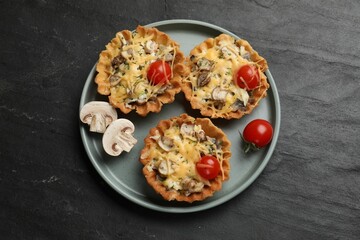 Tasty tartlets with cheese, mushrooms and tomatoes on dark textured table, top view