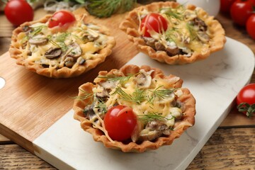 Tasty tartlets with cheese, tomatoes and dill on wooden table, closeup