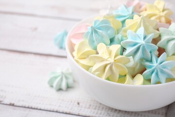 Tasty meringue cookies in bowl on white wooden table, closeup. Space for text