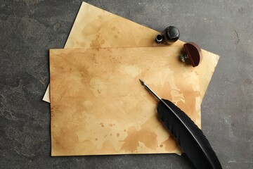 Black feather, inkwell and vintage parchment on grey table, flat lay