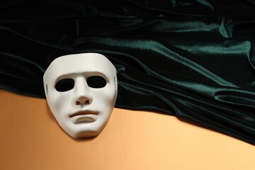 Theater arts. White mask and green fabric on pale orange background, above view