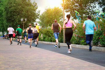 City marathon runners run along a pedestrian path in a city park.