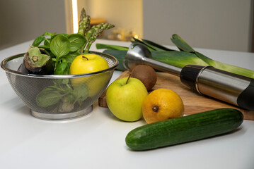 Immersion blender on kitchen table with green vegetables and fruits