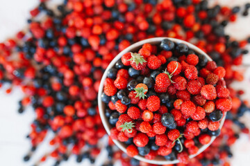 Overhead view of a bowl of fresh strawberries and blueberries overflowing onto a wooden table