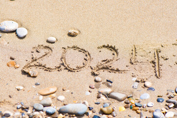 2024 Written in Sand with Pebbles. 2024 written in sand on a beach with pebbles and stones scattered around.