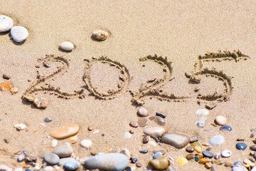 2025 Written in Sand with Pebbles. 2025 written in sand on a beach with pebbles and stones scattered around.