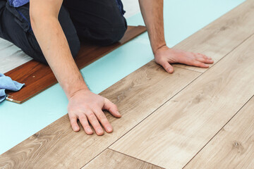 Man laying laminate flooring - closeup on male hands. Worker hands installing timber laminate...