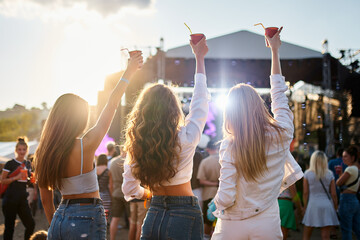 Group of girls at a beach music festival, holding drinks up, enjoying the sunset. Party atmosphere...