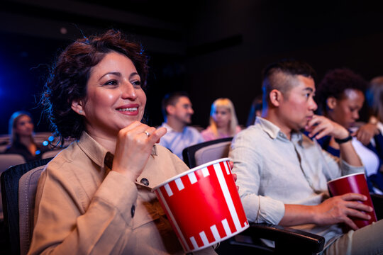 Hispanic woman watching movie in cinema and eating popcorn.