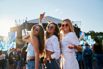 Group of happy young women dancing at sunset beach music fest. Friends in stylish outfits enjoy...
