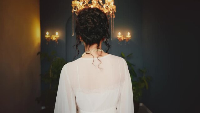woman dark curly elegant hair bun historical updo hairstyle victorian style back rear view. Sexy beauty face red lips eyes girl in luxury room shines. Long vintage white silk dress noble lady art 4k