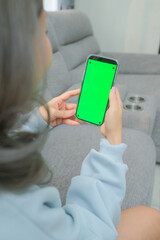 A woman uses a mobile phone or tablet with a green screen to watch videos, surf social media, or have an online conference.