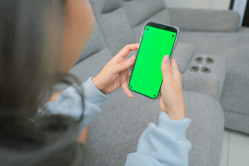 A woman uses a mobile phone or tablet with a green screen to watch videos, surf social media, or have an online conference.