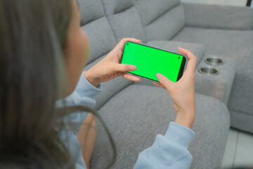 A woman uses a mobile phone or tablet with a green screen to watch videos, surf social media, or have an online conference.