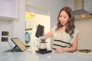 A woman makes coffee and reads the news on a tablet in the kitchen, in a room filled with the aroma of coffee.