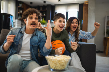 Latino family is watching basketball match and eating popcorn.They are cheering for their team.
