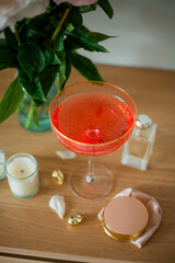 Bouquet of pink peonies in glass vase, candles, glass with pink cocktail, cosmetics, things for women, decorations on wooden table. Spring flowers.