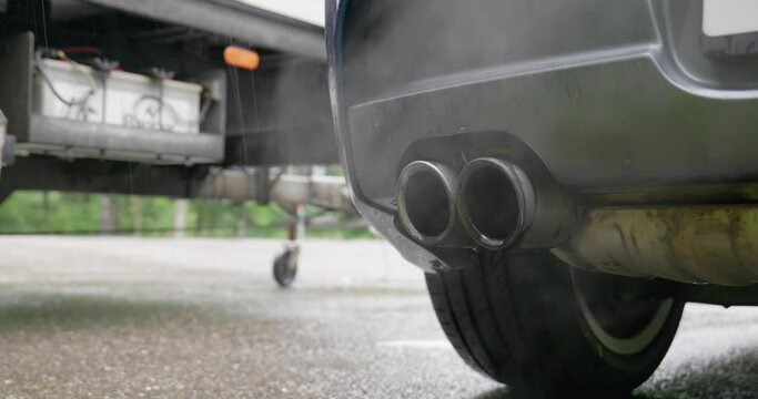 Smoke streams from a car's tail pipe or exhaust tips. Close up, low-angle shot, real time, no people