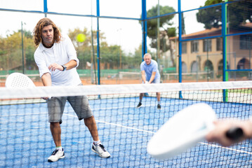 Portrait of focused adult man playing paddle tennis couple match at outdoors court